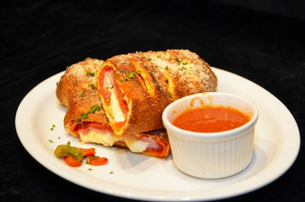 A stromboli sliced open, pepperoni and melted cheese inside, with a cup of marinara for dipping